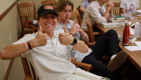 A student at the table gives a double thumbs-up to the camera