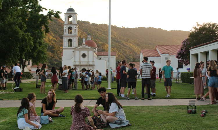 Freshman socialize on the grass by the Commons with the Chapel visible in the background
