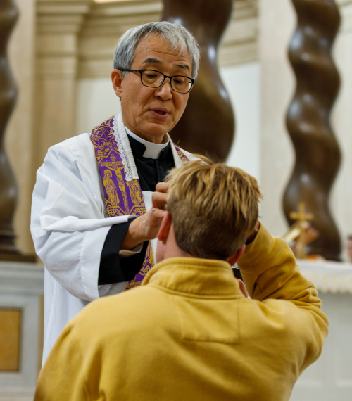 A priest imposes ashes on a student on Ash Wednesday