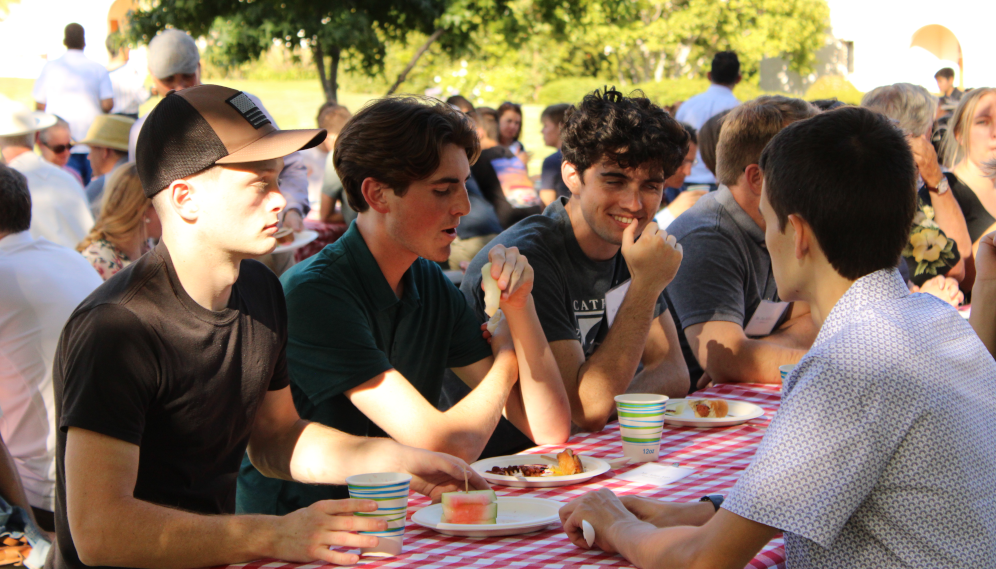 Students dine on hotdogs and watermelon at outdoor picnic tables