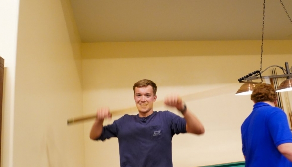 A students waves his pool cue enthusiastically