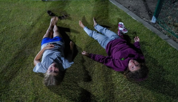 Two lie flat on their backs in the grass at night, stargazing