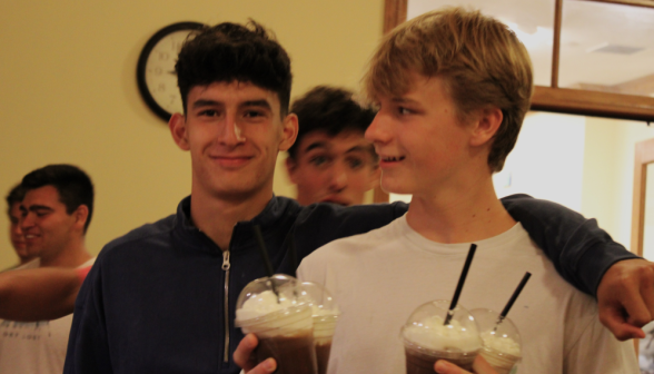 Two students pose for the camera with four drinks in hand