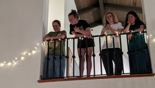 Four spectate from above, leaning over a Christmas light-studded railing