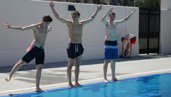Three students balance at the edge of the pool, arms in air
