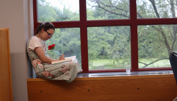 Curled up on a window ledge, a student takes notes with a flower pen