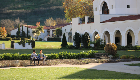 Two students sit on a bench in the quad