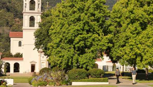 Long shot of two students walking under the trees, with the Chapel dominating the background