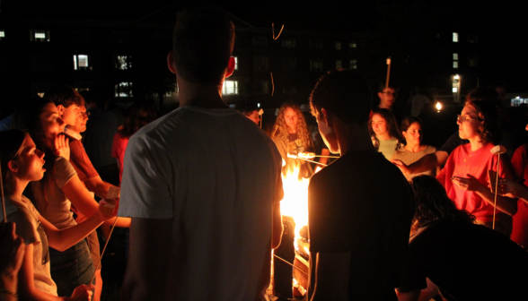 Students around the fire are lit red by its glow