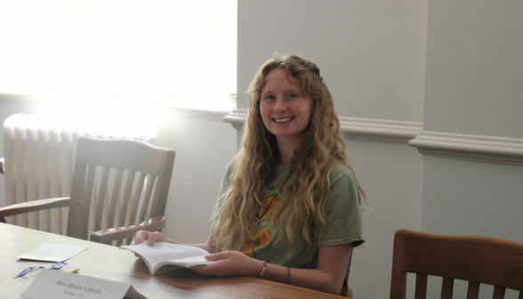 A student studying at a classroom table smiles at the camera