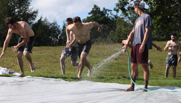 A group of shirtless young men running the spray of a hose.