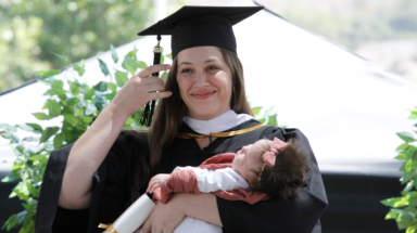 A graduate flips her tassel, newborn in arms