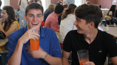 A pair of students at lunch, laughing over orange soda and chicken