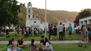 Freshman socialize on the grass by the Commons with the Chapel visible in the background
