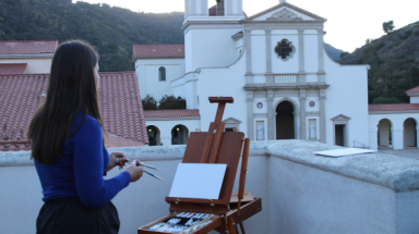 A student paints the Chapel at an easel as the sun sets