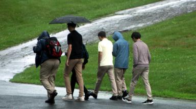Students walk across campus in the rain, carrying umbrellas
