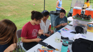 Students do arts and crafts at a shaded outdoor table