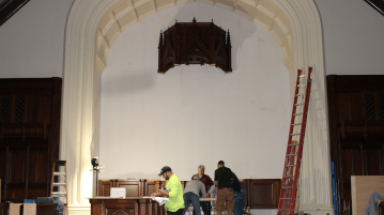 Workers stand under the first piece of the reredos currently
